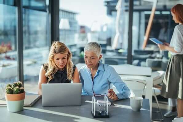 a woman and an elderly woman sitting at a table looking at a laptop.